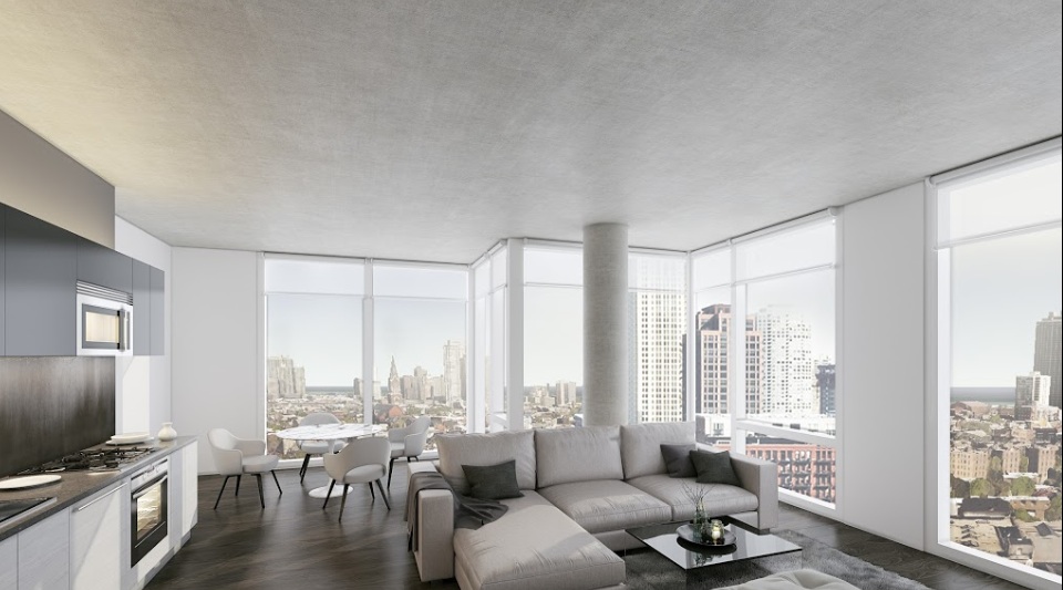 Modern living room with large windows showcasing a city skyline. Features include a corner sofa, coffee table, kitchenette, and a dining area with a round table and chairs.