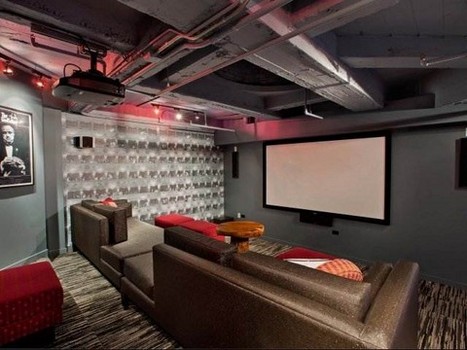 Home theater with gray sofas, red cushions, a large screen, projector, and dim lighting. Wall decor features framed art and a textured panel.