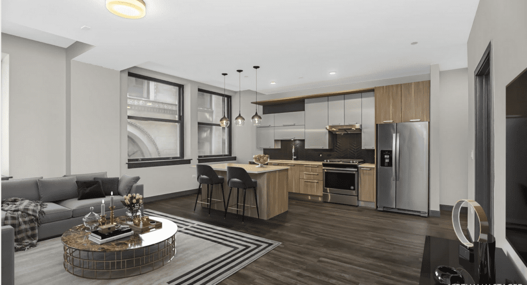 Modern open-concept living room and kitchen with hardwood floors, gray sofa, round coffee table, island with bar stools, stainless steel appliances, and pendant lights.