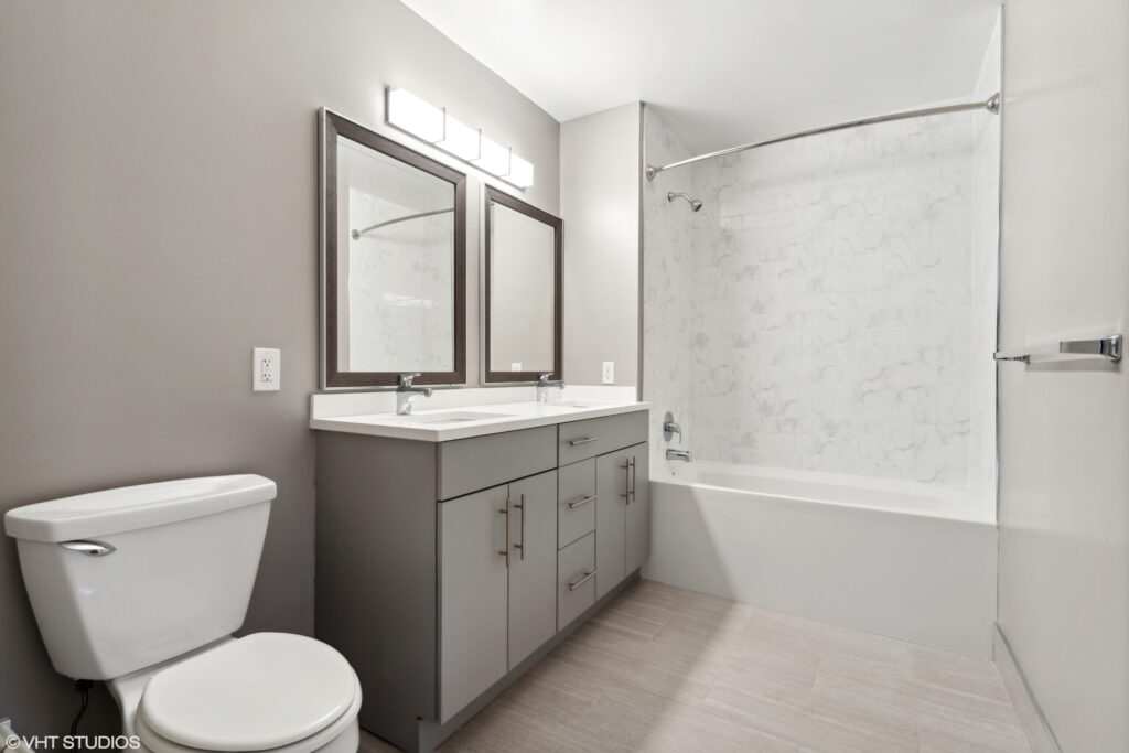 Modern bathroom with gray walls, dual-sink vanity with mirrors, and a bathtub-shower combo.