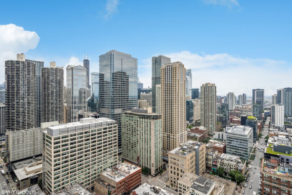 Skyline view of a bustling city with a mix of modern skyscrapers and older buildings under a partly cloudy blue sky.