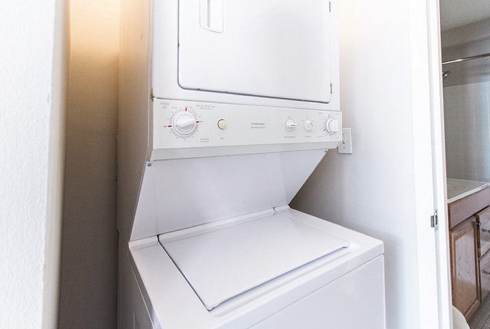 Stacked white washer and dryer unit in a small laundry nook, with visible control dials and buttons.