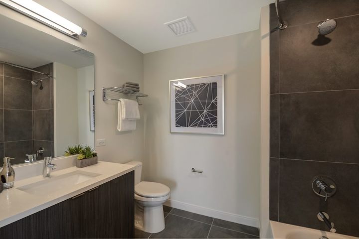 Modern bathroom with a dark vanity, white countertop, mounted towels, abstract wall art, and a shower-tub combination.