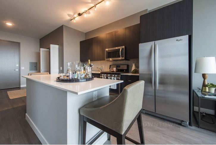 Modern kitchen with a white island, bar stools, stainless steel appliances, and dark wood cabinets under warm lighting.