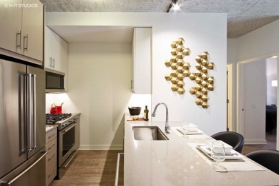 Modern kitchen with sleek appliances, a marble countertop, and geometric wall art. Dining area includes three place settings with black chairs. Neutral color palette with wood flooring.