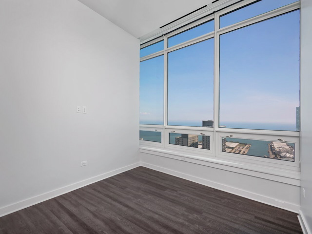 Unfurnished room with large windows offering a view of a cityscape and water. The room has dark wood flooring and white walls.