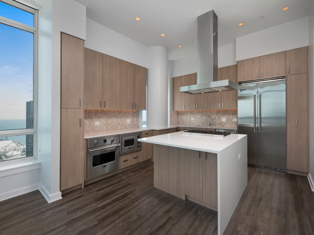 Modern kitchen with wooden cabinets, an island with a stove, stainless steel appliances, and a large window offering a view of the outside.