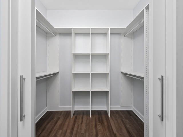 Empty walk-in closet with dark wood floor, white shelving, and hanging rods on three walls.
