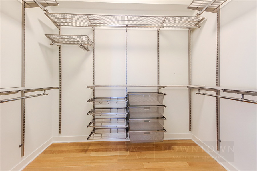 Empty walk-in closet with wooden floor, metal shelves, and multiple storage compartments on white walls.