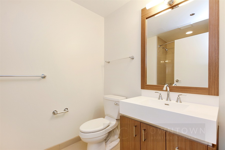 Bathroom with beige tiles, a toilet, a large mirror above a sink with a wooden cabinet, and a towel rack on the wall.