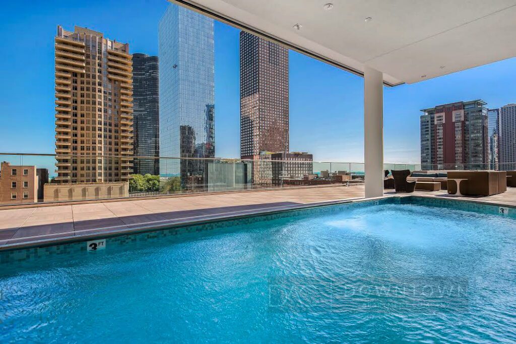 Rooftop pool with a city skyline view featuring tall modern buildings under a clear blue sky.