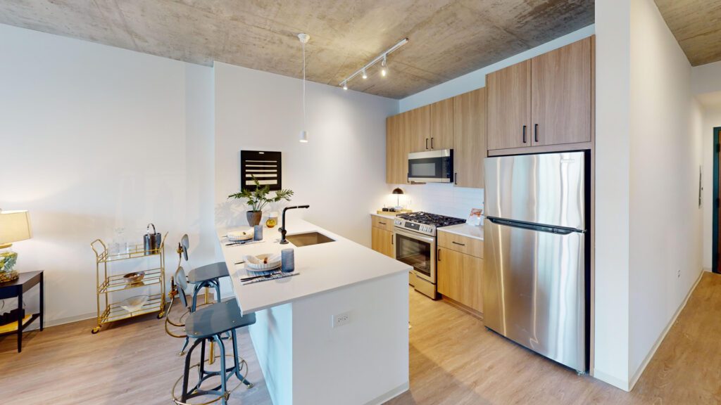 Modern kitchen with wood cabinets, stainless steel appliances, a white countertop island with two stools, and a small dining area set for two.