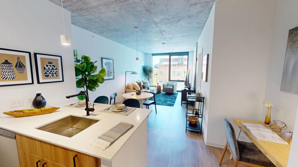 Modern studio apartment with exposed concrete ceiling, open kitchen, dining area, living room, desk workspace, large window, and contemporary decor.