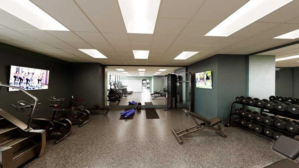 A modern gym room with cardio machines, free weights, benches, yoga mats, mirrored wall, and TVs mounted on the walls.