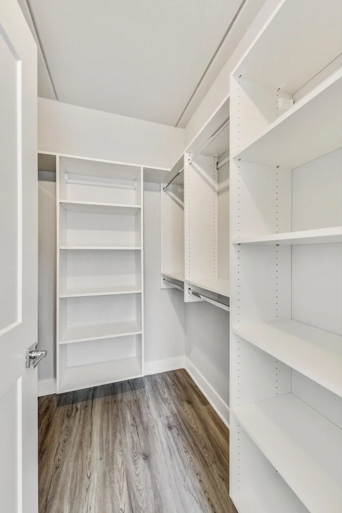 Empty walk-in closet with white shelves, hanging rods, and wood-look flooring, viewed from the doorway.