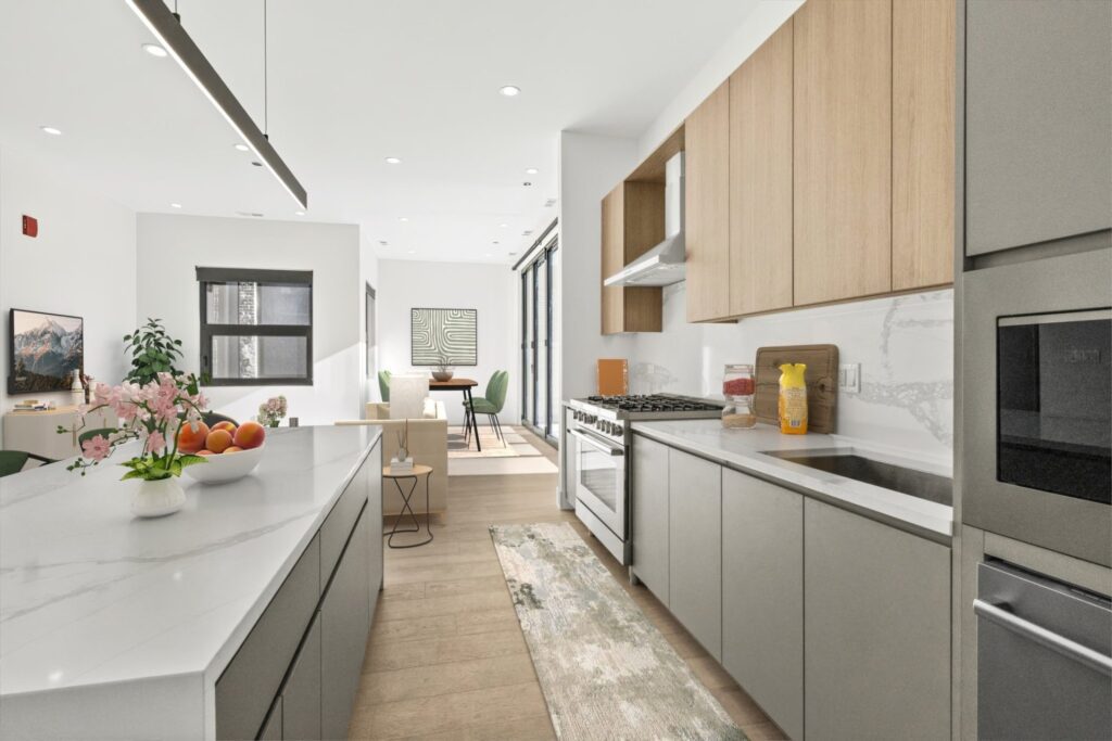 Modern kitchen with light wood and gray cabinets, white countertops, built-in appliances, and a center island. Dining and living areas are visible in the background.