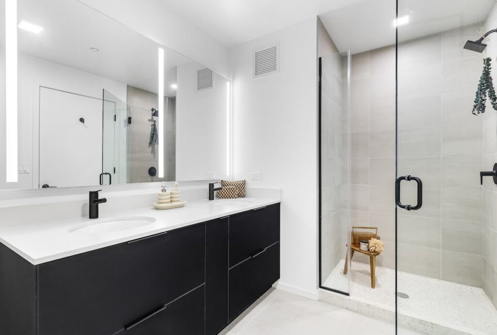 Luxury apartments at The Elizabeth by Sterling Bay. Modern bathroom with a black vanity, double sink, and a walk-in glass shower.