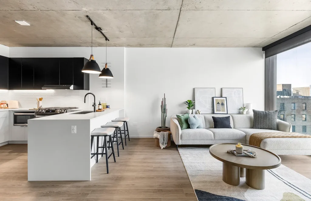 Open-plan kitchen and living room featuring a white island with three stools, a gray sectional sofa, and a low oval coffee table.