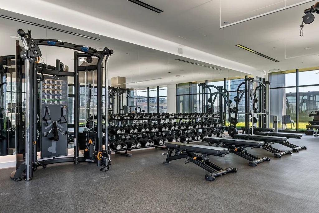 Luxury apartments at The Elizabeth by Sterling Bay. Gym interior with a cable machine, racks of dumbbells, and several weight benches.