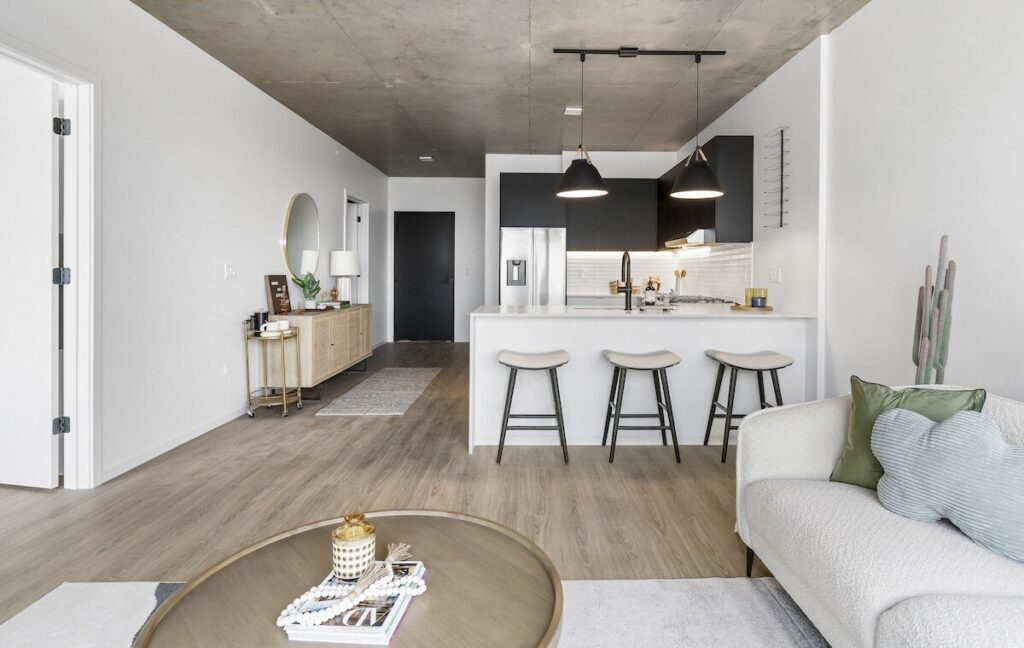 Luxury apartments at The Elizabeth by Sterling Bay. A modern apartment interior featuring an open kitchen with a breakfast bar, three stools, and an adjacent living area with a sofa and coffee table.